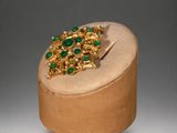 gold and emerald broochle on a wooden box on a grey background