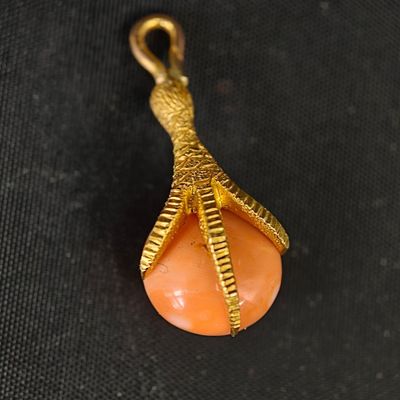 une photo d'un pendentif aux couleurs or et corail posé sur un tissu noir