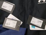 three men ' s under armour jackets with tags on them sitting on a bed