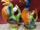 pair of colorful ceramic rooster vases sitting on a tile floor
