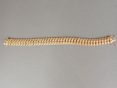 gros plan d'un bracelet en chaîne en or sur une surface grise