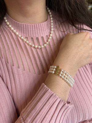 une femme portant un pull rose, des bracelets en perles et un collier de perles