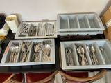 Plusieurs plateaux d'argenterie sont posés sur une table noire entourée de chaises rouges.