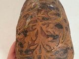 a hand holding a brown vase with designs on it