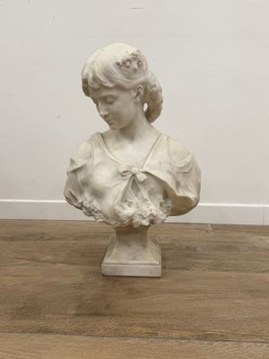 buste en marbre représentant une femme avec une fleur dans les cheveux, posé sur un parquet