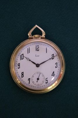 une montre de poche en or avec un cadran blanc, posée sur un tissu vert