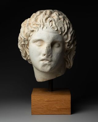 une tête de femme en marbre blanc aux cheveux bouclés, posée sur un socle en bois
