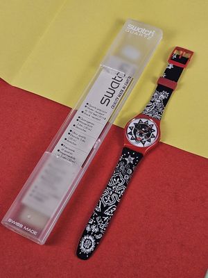 a black and white watch sitting next to a red and yellow piece of paper