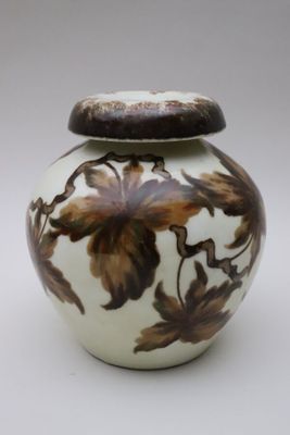 un vase blanc orné de fleurs marron, posé sur un fond blanc