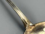 une cuillère en argent avec un manche, posée sur une surface grise
