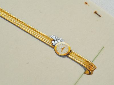 une image représentant une montre en or posée sur une surface blanche, ornée d'une fleur