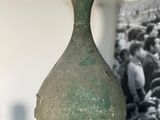 un vase vert posé sur une étagère, avec une photo en arrière-plan