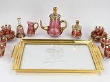 un plateau en or sur lequel est posé un service à thé en verre rose