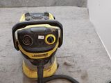 L'aspirateur jaune et noir est posé par terre, près du mur.