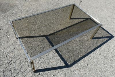 une table en verre avec un piètement en métal, posée à même le sol
