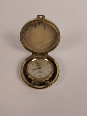une petite montre de poche en or posée sur une surface blanche