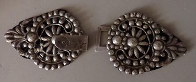 pair of silver plated brooches on a white surface