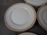 four white and gold plates with gold trims on a table