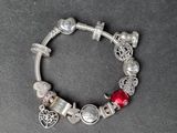 a close up of a silver bracelet with red beads and charms