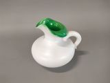 a small white vase with a green leaf on it