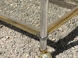 a metal and glass coffee table with wheels on the ground