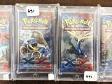 trois paquets de cartes à collectionner Pokémon dans des pochettes en plastique, posés sur une table