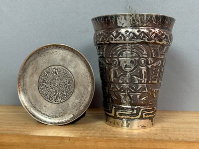 un vase en argent posé sur une table en bois, à côté d'une assiette en argent