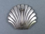 a silver shell shaped brooch with a cross on it