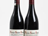 two bottles of red wine sitting next to each other on a white surface