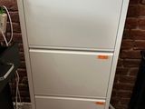 a white filing cabinet with three drawers next to a brick wall