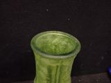 a green vase sitting on a table next to a black wall