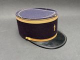 chapeau violet orné d'une bordure dorée, posé sur une surface grise