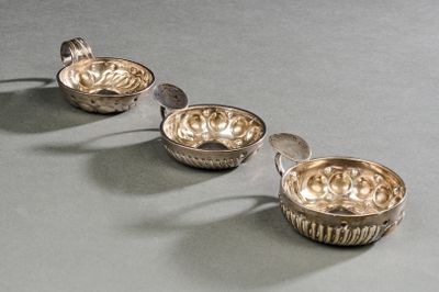 trois plats en argent accompagnés de cuillères, posés sur une table devant un fond gris