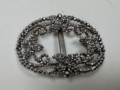 une broche en argent ornée de perles, posée sur un fond blanc