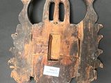 an old wooden mask hanging on a wall with a tag attached to it