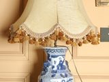 un vase bleu et blanc posé sur une table, sur laquelle se trouve une lampe