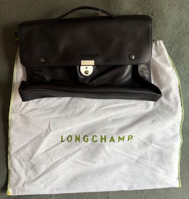 un sac Longchamp noir posé sur un sac blanc, lui-même posé sur un tapis vert