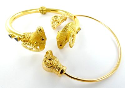 deux bracelets en or ornés de breloques en forme de poisson, posés sur un fond blanc