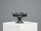 a black bowl sitting on top of a white pedestal next to a gray wall