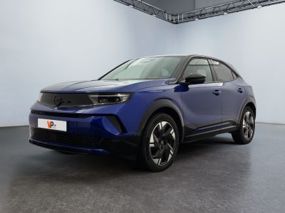 Une voiture bleue est garée dans une grande pièce aux murs blancs.