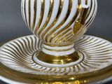 a white and gold vase on a saucer on a plate