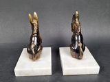 two statues of rabbits sitting on marble blocks on a gray surface