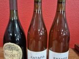 three bottles of wine sit on a wooden table in front of a red wall