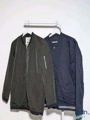 two jackets hanging on a clothes rack against a white wall