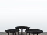 deux tables noires posées sur un sol en béton, près d'un mur blanc