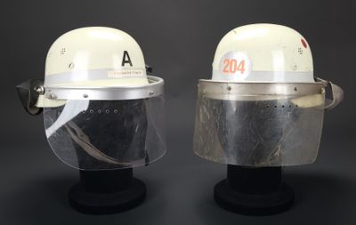 une paire de casques blancs avec des visières transparentes, posés sur des supports, sur fond noir