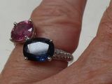 a woman ' s hand holding a ring with two different colored stones on it
