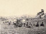 many men standing and sitting in a field with animals