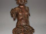 une vieille statue en bois représentant un bébé assis sur une surface blanche