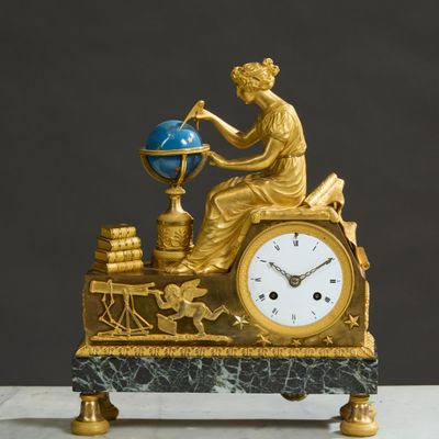 a gold clock with a woman sitting on top of it